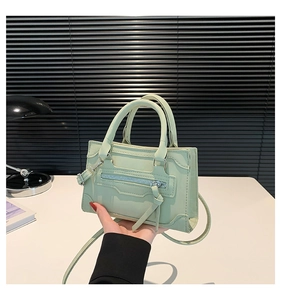 Detail of mint green leather crossbody bag with dual handles and stylish tassel zipper