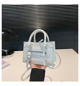Close-up of white leather handbag featuring moto-style zippers and decorative tassels