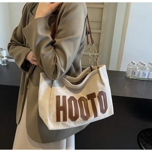 Detail of canvas tote bag featuring brown leather HOOTO lettering and gold chain strap