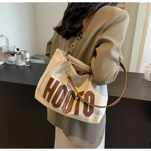 Close-up of canvas tote bag with brown HOOTO patch and chain link leather shoulder strap