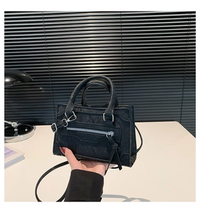 Detail view of black faux leather handbag showing unique pleated texture and silver zippers