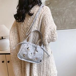 Elegant grey drawstring bucket bag with gold butterfly charms shown in a lifestyle interior