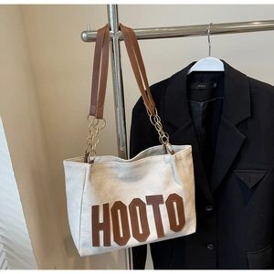 Detail of canvas tote bag featuring brown leather HOOTO patch and metal chain strap
