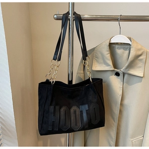 Detailed close-up of a black suede tote bag featuring leather HOOTO letters and gold chain strap