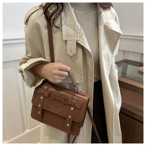 Detalle de bolso bandolera marrón en ecopiel con adornos de corazón y lazos en gabardina