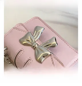 Detail view of pink leather bag featuring a large silver metal bow and chain strap