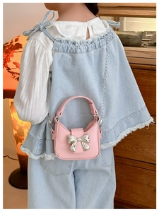 Detailed view of kids pink leather bag with a large silver bow and chain strap