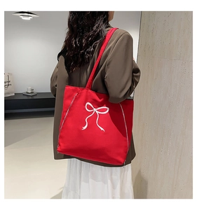 Détail du sac cabas rouge en toile avec broderie nœud et zips latéraux par mannequin