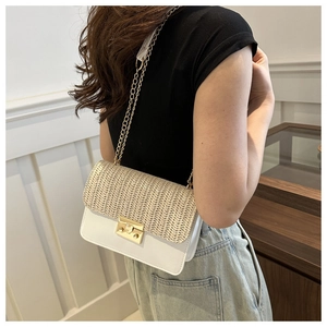 Detail of the woven straw texture and white leather flap with golden chain strap and buckle