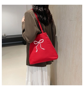 Détail du sac cabas en toile rouge avec un nœud blanc brodé sur une surface texturée