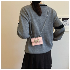 Pink crossbody bag with silver bow detail and chain strap worn by a model over a skirt
