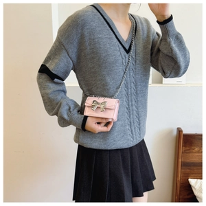 Detail of pink patent leather crossbody bag with silver bow decoration on grey sweater