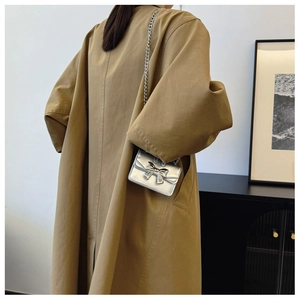 Silver chain handbag with bow detail worn over a khaki trench coat by a model