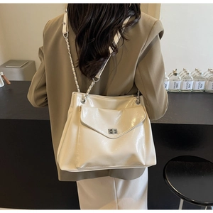 Rear view of a model wearing a chic beige leather shoulder bag with a metal twist lock