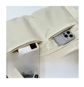 Detail view of cream nylon crossbody bag featuring two front zipper storage pockets