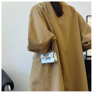 Detail of silver crossbody bag featuring a 3D bow design and slender metal chain strap