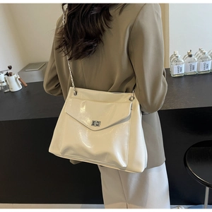 Chic cream glossy leather shoulder bag featuring a silver metal chain strap on a blazer