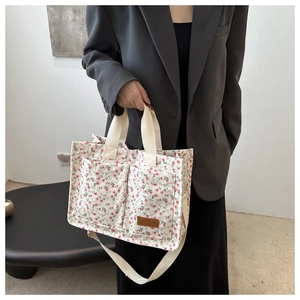 Detail of floral canvas tote bag showing dual front pockets and brown fashion leather tag