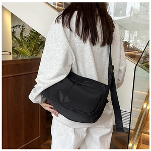 Macro detail of a large black nylon crossbody bag showing the durable fabric and wide strap