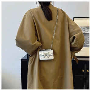Silver metallic crossbody bag featuring a bow detail and chain strap worn by a model