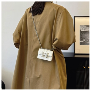 Detail of white mini crossbody bag with silver metal bow and delicate chain strap