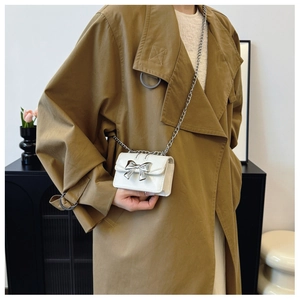 Close-up of mini white crossbody bag with silver bow buckle and chain on trench coat