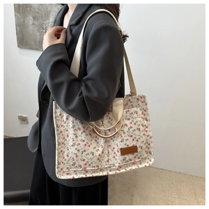 Detail of floral canvas tote bag with brown leather label worn over a grey blazer