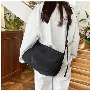 Close-up of minimalist black nylon crossbody bag with dual zippers on a white outfit