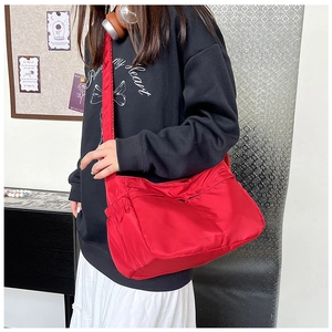 Detail view of red nylon tote bag featuring functional drawstring side pocket and zippers