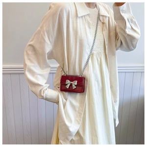 Detail of red mini crossbody bag with silver bow ornament and slim metal chain strap