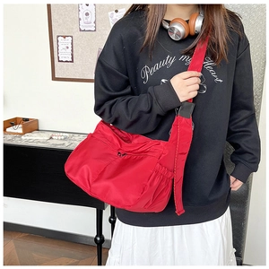 Detail view of a red nylon crossbody bag with multi-pocket design on a casual outfit