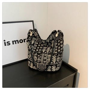 Détail du sac seau à imprimé floral avec lanières noires et boucles dorées sur une table