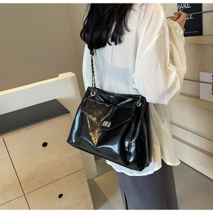 Detail view of large black glossy leather tote bag with silver chain and metal clasp