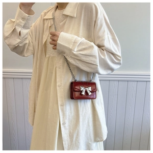 Detail of red mini chain bag featuring a metallic silver bow and glossy patent finish