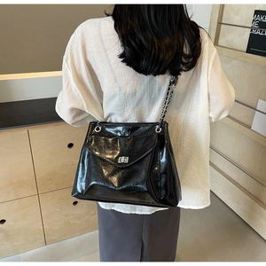 Black glossy shoulder bag with silver turn-lock buckle and chain strap on a model back