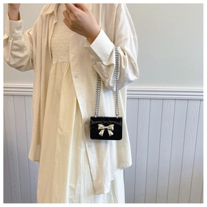 Detail view of mini black patent leather square bag with silver metal bow and chain strap