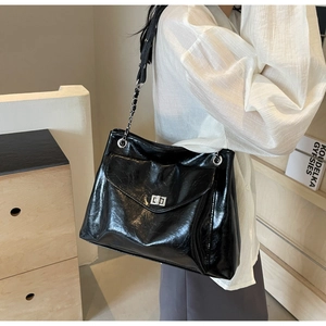 Close-up of black glossy patent leather shoulder bag with silver turn-lock and chain strap