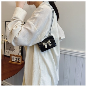 Detail of micro black patent leather bag with silver bow accent and metal chain strap