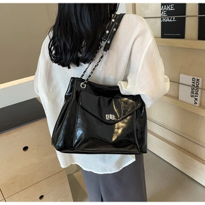 Detail view of black glossy tote bag with silver square twist lock and chain strap