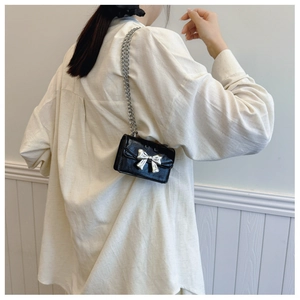 Mini black crossbody bag with silver bow detail shown on a model for styling