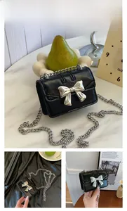 Detail of black mini crossbody bag featuring a silver bow buckle and metal chain strap