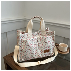 Detail view of floral canvas tote bag featuring double front pockets and leather logo tag