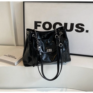Detail of a large black tote bag with glossy leather texture and silver twist-lock buckle