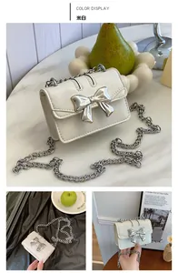 Detail shot of a cream white mini crossbody bag featuring a large silver metal bow accent