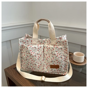 Close-up of floral canvas tote bag with front pockets and brown leather brand label