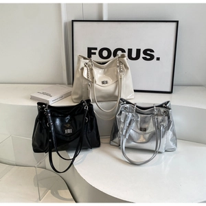 Close-up of three glossy tote bags with metal chain straps and twist locks on steps