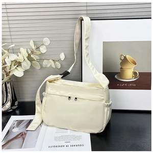 Detailed view of cream nylon shoulder bag with dual front zippers and side pocket details