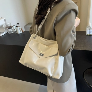 Large cream white shoulder bag with metal lock and chain strap on a model in a cafe