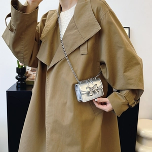 Silver metallic mini crossbody bag with bow detail and chain strap on trench coat model