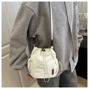 Detail showing white nylon bucket bag with mesh side pocket and fashion label on shoulder
